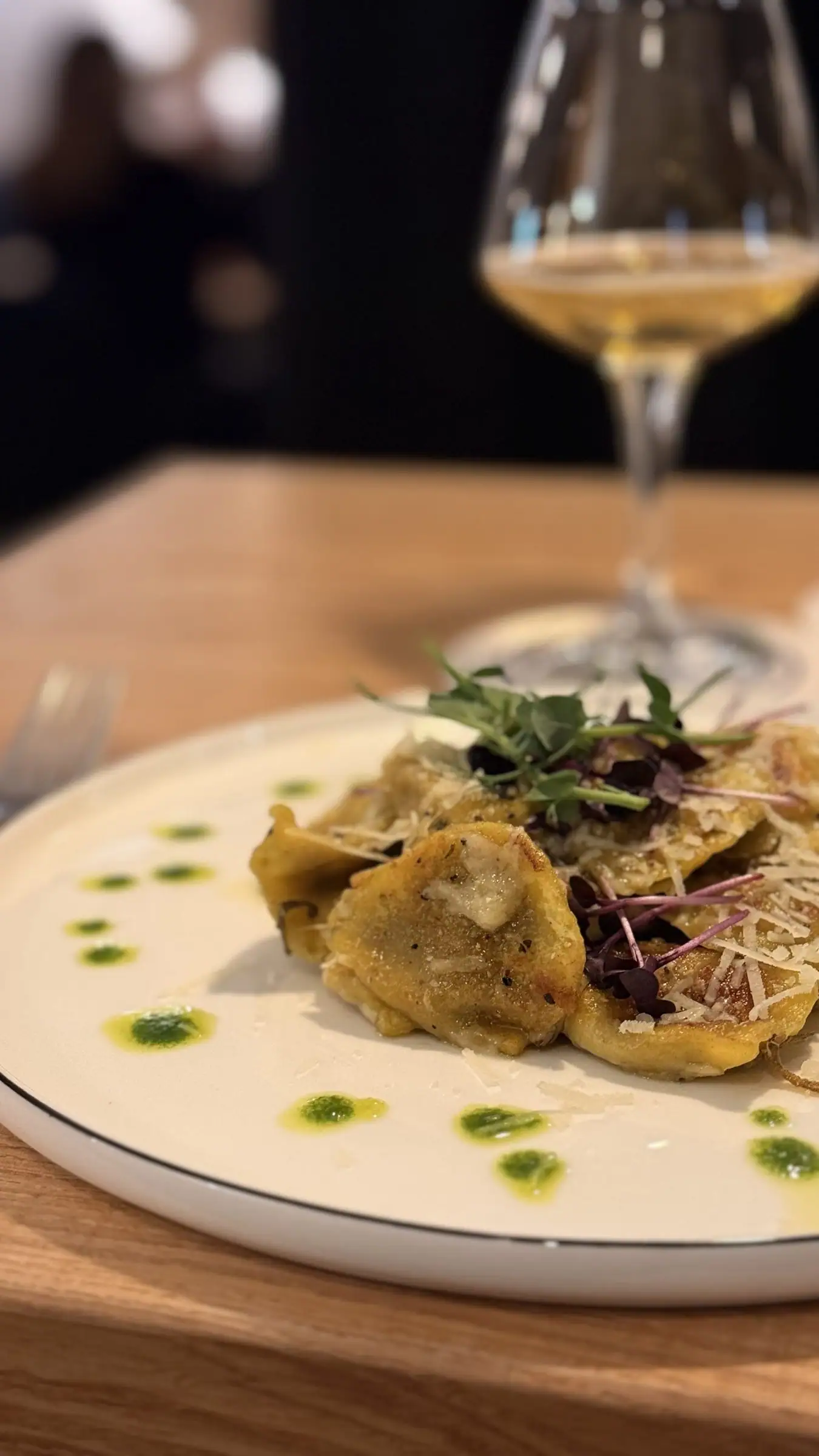 Filled pasta with parmesan and herb oil, a glass of white wine behind